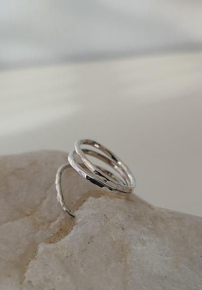 a double banded silver ring with hammered and glossy effects. it's placed on a pebble