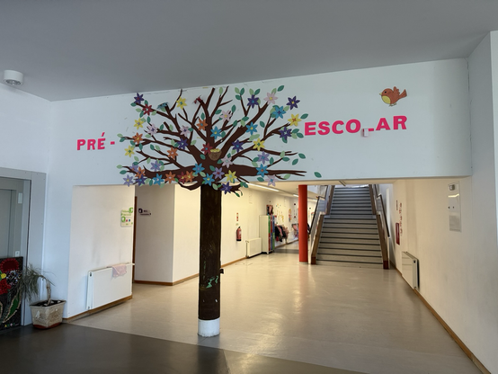 Ikastetxe zuri bat, erdian zutabe bat dauka zuhaitza itxuragaz.