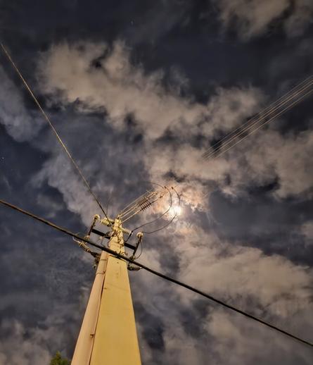 Late night looking up an electrical utility pole, with wires high above illuminated by the moon's glow.