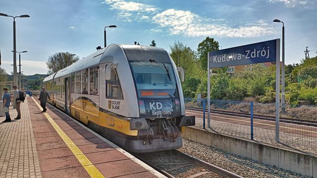 Biało-żółty szynobus Kolei Dolnośląskich na stacji w Kudowie-Zdroju w słoneczny dzień.