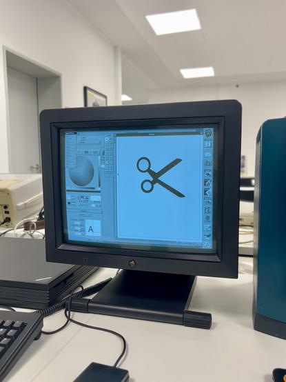 A vintage computer monitor displays an icon of scissors on its screen, surrounded by a workspace with design software and a keyboard. The background features a bright, modern office environment.