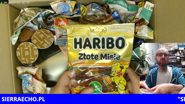 Rzut oka kamery ;) na zawartość jednej z paczek rozpaczkowanych podczas programu LAJW na kanale Sierra Echo. Na pierwszym planie paczka żelków Haribo Złote Misie, w tle ekspres do kawy Nescafe Dolce Gusto, kilka kapsułek tej samej marki, i wypełniacz z kilku kartek gazetki Lidla.