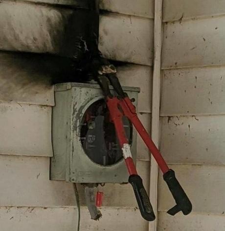 a pair of bolt cutters above a power meter, the siding of the house where they've attempted to cut mains power is blackened with fire because this was a very poor choice