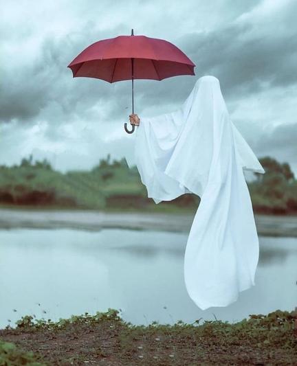 Un lenzuolo dal quale sbuca un braccio che tiene un ombrello rosso. Sullo sfondo uno specchio d'acqua, le colline e un cielo nuvoloso che promette pioggia.