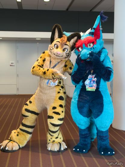 A yellow serval fursuiter and a cyan kobold fursuiter.