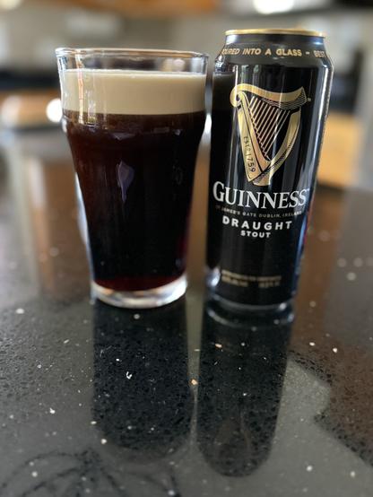 A pint glass of dark beer with a tan head. A black pint can of Guinness draught is to the right, with its shiny golden harp logo