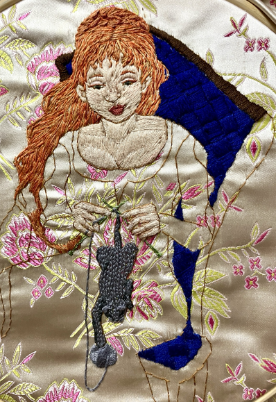 An embroidered panel on progress of a red haired, pale skinned woman knitting a grey kitten, sitting in a cobalt blue tufted chair.