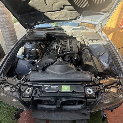 A view into the engine compartment of my blue 2003 BMW 530iT wagon, where the freshly installed M54B30 inline six-cylinder engine has been nearly fully dressed with new cooling system components and the air filter housing, though the latter is not yet bolted down.