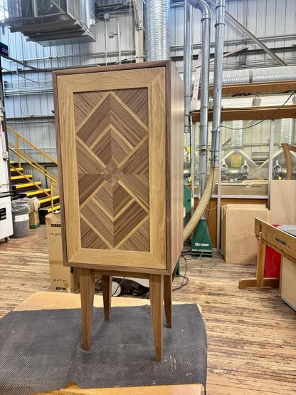 The front of a Walnut and White Oak Veneered cabinet with solid walnut legs and a door panel that is in a art deco parquetry style.