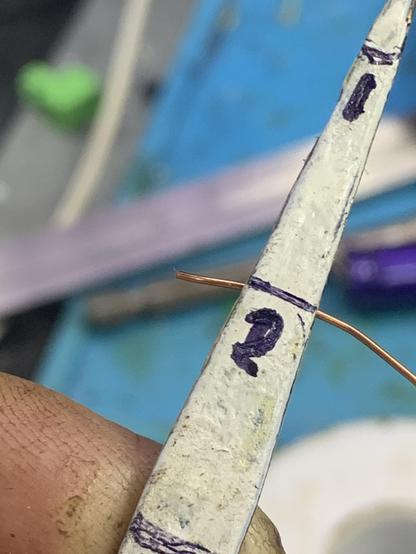 A piece of wire held in tweezers at the “two” marker
