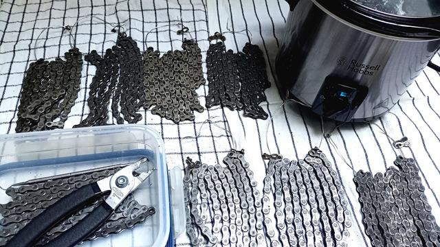 Mehrere Fahrradketten liegen auf weißen Handtüchern neben einer Plastikdose mit Kettenzange und eine Schongarer.