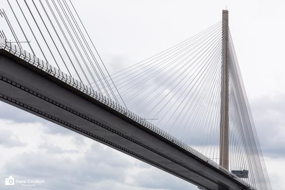 A photograph of the Queensferry Crossing bridge across the Firth of Forth. Shot from a boat on the water for a different perspective on a cloudy day.