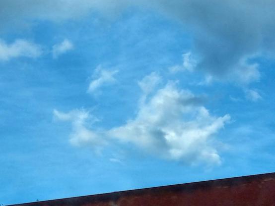 Nel cielo azzurro, sopra un tetto, una nuvola sembra avere la forma di un dragone