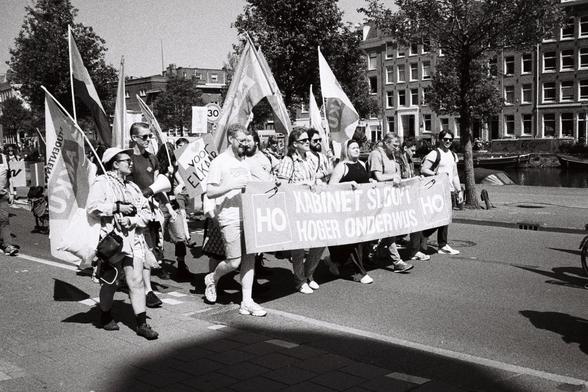 B&W image worker unions demonstrating on May first slogan on sign ¨Voor Elkaar" (for each-other ), banner "Kabinet sloopt hoger onderwijs¨ (kabinet destroys higher education), flags with AKKU, student workers union