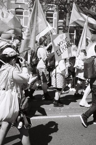 B&W image worker unions demonstrating on May first slogan on sign ¨Voor Elkaar" (for each-other ), Palestinian flag, student workers union AKKU flags, photographer in left front of frame.