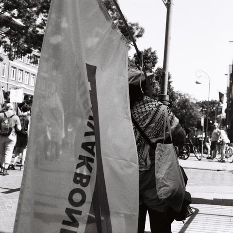 B&W image worker unions demonstrating on May first union member with AKKU flag observing bystanders and march, student workers union, bystanders unsharp in background
