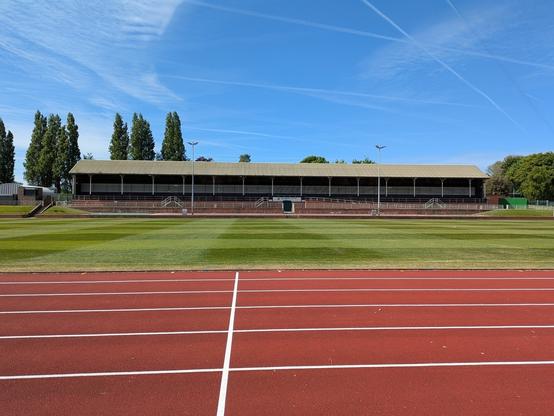 A running track leads to a grandstand set against a clear blue sky and surrounded by trees.