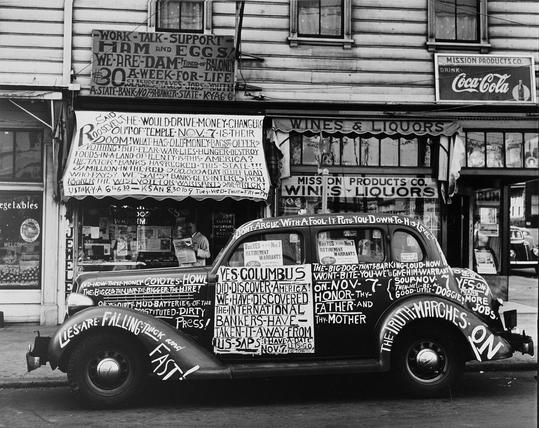 A black and white photo from 1939 showing a car completely covered in political slogans, including ones inveighing against a dirty press, international bankers, and arguing with fools.