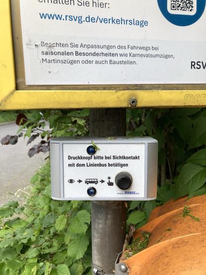 Hier gibt es ein Ding zu sehen, auf dem steht; Druckknopf bitte bei Sichtkontakt mit dem Linienbus betätigen. Darunter ist ein Auge abgebildet, dann folgt ein Pfeil, dann ein Linienbussymbol, dann eine schwarze Hand deren Zeigefinger auf den Druckknopf tippt. Daneben befindet sich dann ein dicker schwarzer echter Druckknopf. Das Ding ist unter dem Busfahrplan am Pfahl montiert.