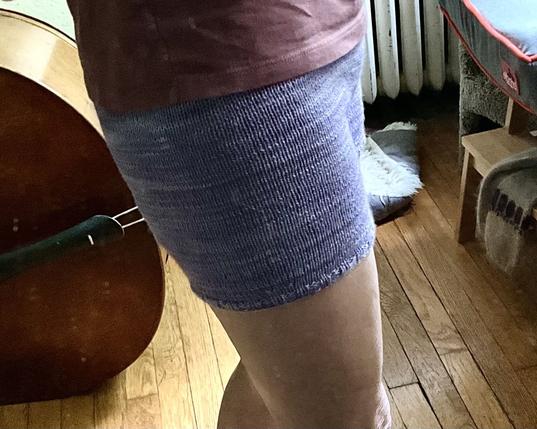 side view of purple knitted shorts, mirror shot on author, includes top of legs, bottom of muted pink t shirt, double bass musical instrument partial view on floor
