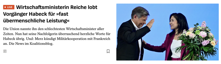 Wirtschaftsministerin Reiche und ihr Vorgänger Robert Habeck stehen nebeneinander auf einer Bühne. Reiche überreicht ihm einen großen Blumenstrauß und lächelt dabei, während Habeck mit gesenktem Kopf und einem angedeuteten High-Five reagiert. Daneben die Schlagzeile: „Wirtschaftsministerin Reiche lobt Vorgänger Habeck für ‚fast übermenschliche Leistung‘“.