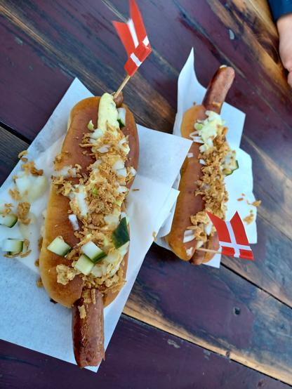 elaborately loaded pølser (Danish hotdogs) resting of paper napkins and piled high with remoulade and ristede løg  (fancy mayo and crispy onions), topped with little Danish flags on toothpicks.