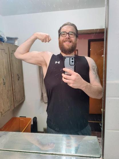 A photo of me flexing my left bicep in the mirror from May 2025. The mirror is still pretty dirty.