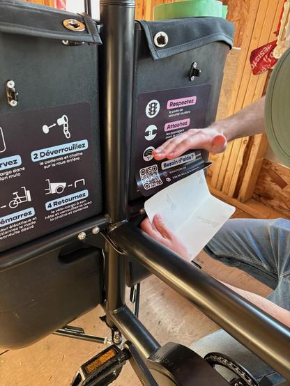A hand that is sticking a decal in a cargo bike box / Une main en train de coller un autocollant sur la boîte d'un vélo-cargo.