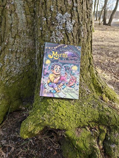 Kuvassa Myrtti ja kudelmataika -kirja kuvattuna puuta vasten.