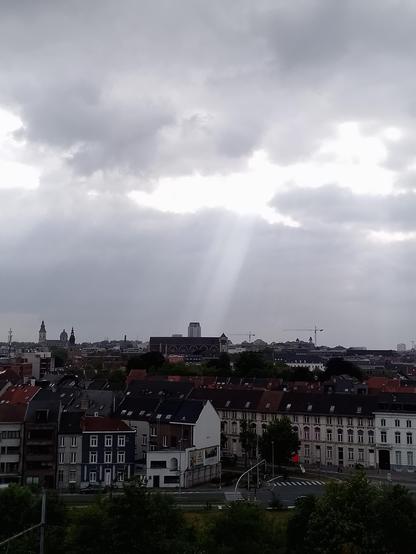 Een panorama van Gent onder een bewolkte hemel. De boekentoren wordt verlicht door een lichtstraal