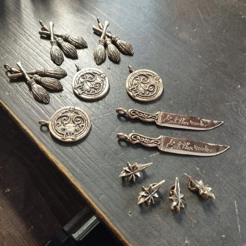 Colgantes de bronce. Tres con la forma de tres escobas. Tres más en forma de puertas de smial, dos chuchillos inspirados en la serie Hannibal, donde se lee en la hoja "Eat the rude", y cuatro mini estrellas de 8 puntas.