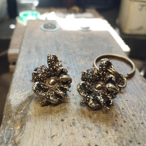 Colgante y llavero de bronce. Son ma misma pieza. Un dado de 10 caras por un lado, por el otro emerge una criatura tentacular lovecraftiana con un ojo en el centro de los tentáculos.