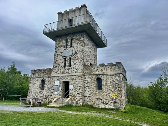 Steinerner Aussichtsturm mit mehreren Plattformen umgeben von grünen Wäldern