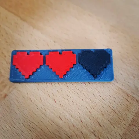 Face du badge représentant 3 cœurs, 2 rouges et 1 noir, de façon pixelisé.