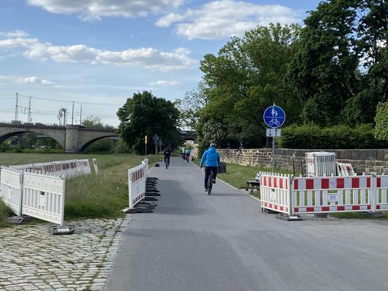 Schilder und Baustellenzäune entlang der Straße des Elberadwegs. Viele Fahrräder sind unterwegs.