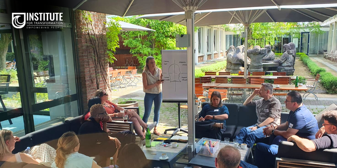 Karen is showing insights out of the agile mindset research at a flipchart. Surrounded with people sitting in a beer garden at the agile coach camp cologne.