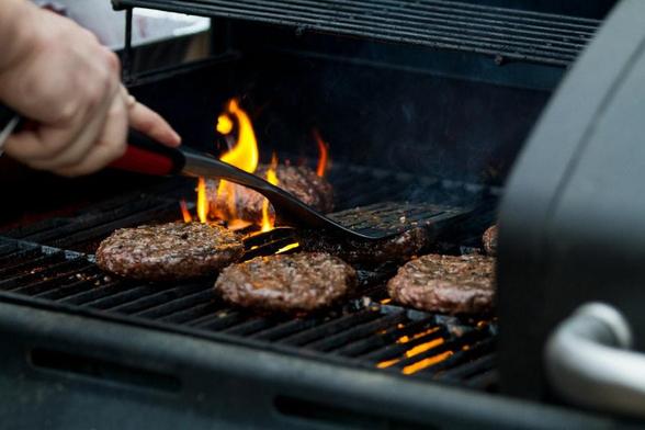 The grillmaster tends to burgers on a flaming grill.