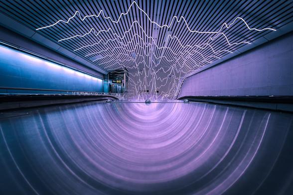 Reflection of zigzagging pink neon lights on a shiny surface of an escalator at Odenplan metro station in Stockholm.