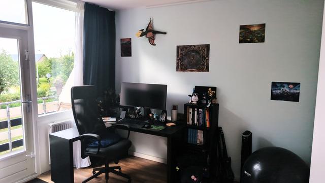 An at home workplace containing a desk with chair, a widescreen monitor, other computer stuff, a small bookcase with some books, and lots of merch from games and other nerdy stuff including multiple The Elder Scrolls items as well as some Vocaloid, Spyro, OS・SCi, OWASP, some Nintendo game & watches, and some other stuff.