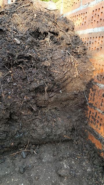 Ein angestochener Komposthaufen. Rechts ein Teil einer Mauer aus querliegenden Lochziegeln. Sehr deutlich zu sehen wie das Substrat von oben nach unten immer feiner wird.