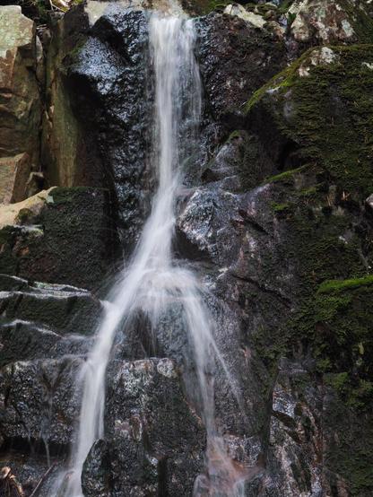 Waterfall coming down the moss covered rockwall. Halfway point the water coming down hits a rock and it spreads around.