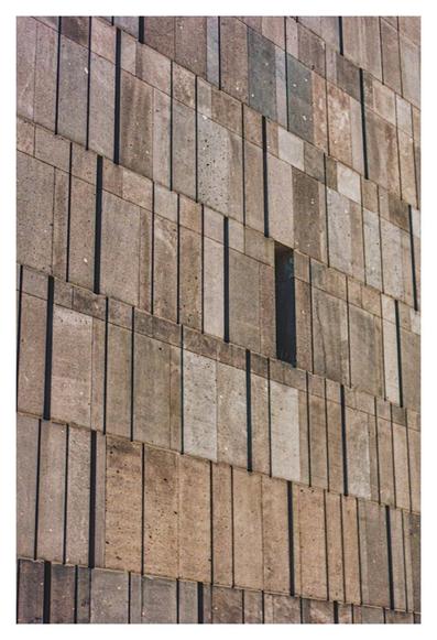 Color photograph of the facade of the Mumok Vienna in the morning light. You can see the stone façade made of basalt lava, which is closed except for a slit of light.