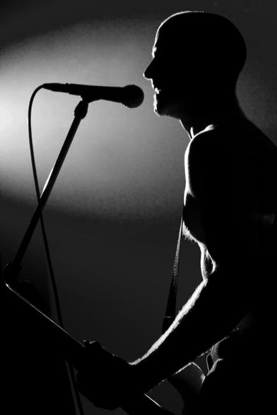 Black and white. Portrait format. Concert of a German punk, rock and pop band. Backlit shot of the singing guitarist.