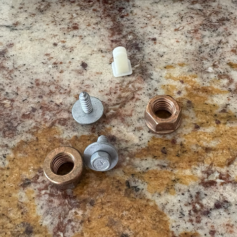 A white plastic expanding nut, two silver screws with washers, and two copper nuts sit on my brown granite kitchen counter.