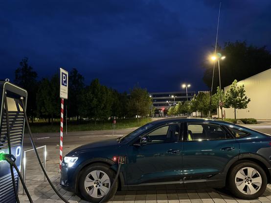 auto am schnellader angeschlossen bei nacht. auf dem auto eine 3m antenne. der ladeport am auto zeigt ein rotes licht