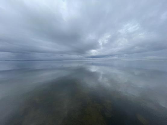 A photo of an expanse of still water with a variegated but predominantly grey sky above it.