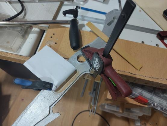 Piece of a silver wooden fantasy sword clamped to a workbench. It has a slot of which one side is protected by paper and the other side is full of dust.