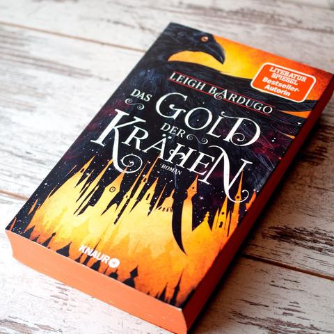 Buch "Das Gold der Krähen" von Leigh Bardugo, erschienen bei Knaur, liegend von schräg oben fotografiert auf weißem Untergrund