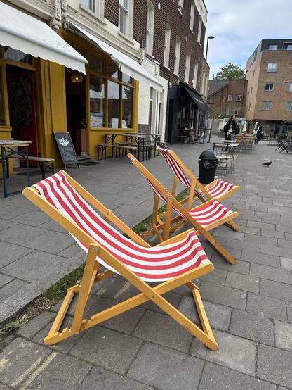 Blue skies over a pedestrianised street; three striped deckchairs in the foreground