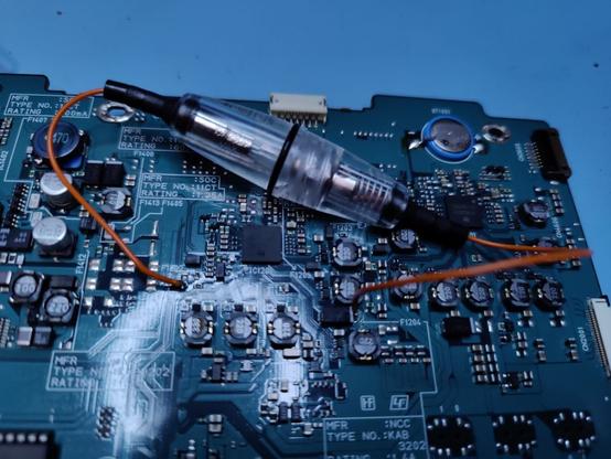 A PCB with quite a few tiny components amidst a few that are larger, yet still below 1cm in diameter. Across lies an in-line fuse holder with the wires soldered to two points on the PCB. The fuse holder could probably contain all the components on the board...